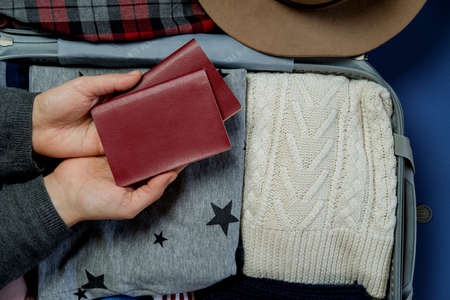Woman hands with passports on the background Open suitcase packed for travelling. Winter vacations...
