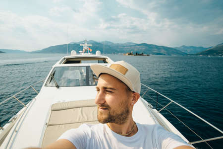 Young man in a cap makes selfie against a yacht in the summerの写真素材
