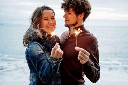Back view of young beautiful happy couple holding sparkles against the sea. の写真素材