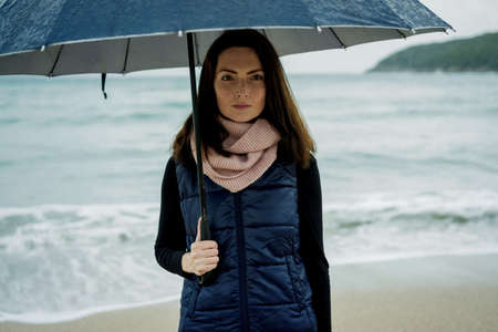Young woman standing with an umbrella in front sea in winter or autumnの写真素材