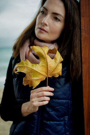 Beautiful Woman with Autumn Leaves against the sea in rainy day