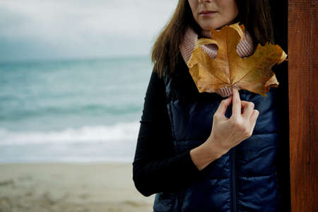 Young Woman with Gold Autumn leaf against the sea in rainy day