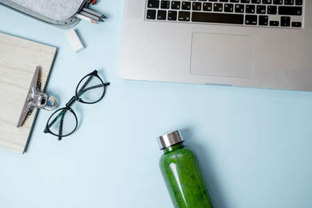 Healthy working life style. Laptop with stationery and green smoothies with apple on blue table. Top view, flat layの写真素材