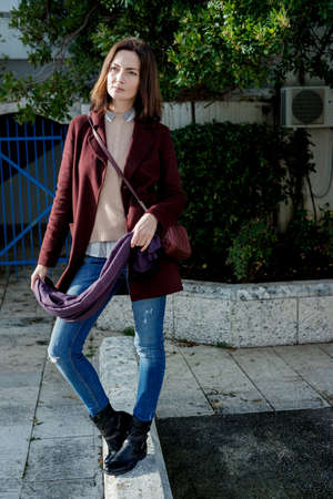 Trendy Young woman in a stylish burgundy coat in the spring walking outdoors
