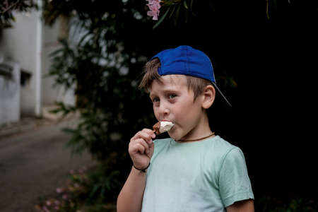 Cute Boy in a blue cap eating an ice cream in the summer against a nature backgroundのeditorial素材