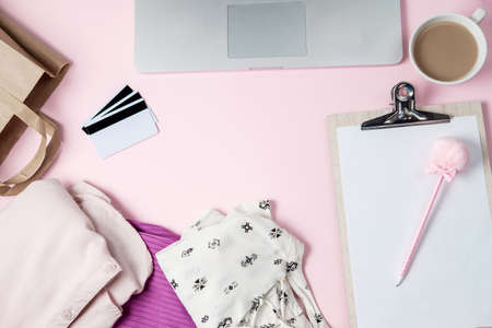 Online shopping background with computer, clothes, credit card on pink table. Flat lay, top viewの写真素材