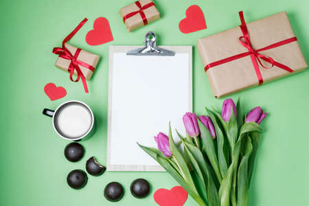 White empty blank, purple tulips and a cup of coffee on a green background. Top view, flat layの写真素材