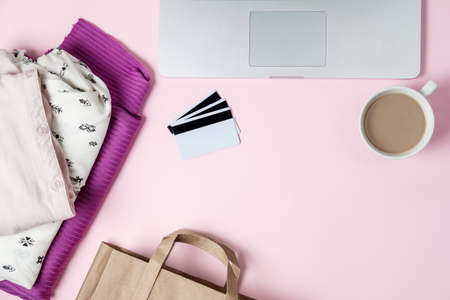 Online shopping background with computer, clothes, credit card on pink table. Flat lay, top viewの写真素材