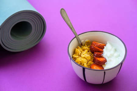 Blue mat for yoga and yoghurt with strawberries and fruits on a purple backgroundの写真素材