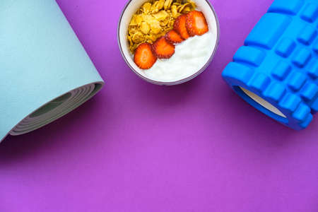 Blue mat for yoga and yoghurt with strawberries and fruits on a purple backgroundの写真素材