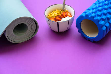 Blue mat for yoga and yoghurt with strawberries and fruits on a purple backgroundの写真素材