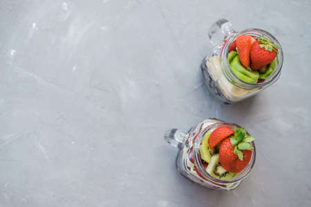 Fresh sliced fruit in a jar: strawberry, cherry bananas and blueberries on a gray background. Useful snack.の写真素材