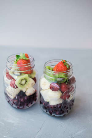 Fresh sliced fruit in a jar: strawberry, cherry bananas and blueberries on a gray background. Useful...