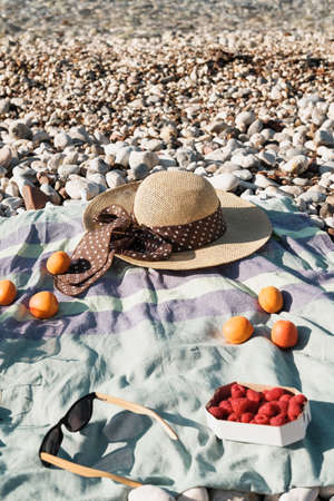 Summer composition with hat, berries and sunglasses on a pebbles beach near sea