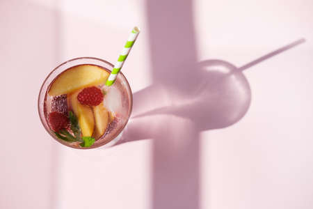 Homemade iced lemonade or tea with ripe peaches and Raspberries. Pink background. Top view, space for textの写真素材