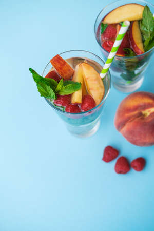 Homemade iced lemonade or tea with ripe peaches and Raspberries. Blue background. Top viewの写真素材