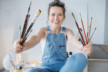 Female artist hand painter with brushes in front of the canvas and drawing. Artist studio interior....