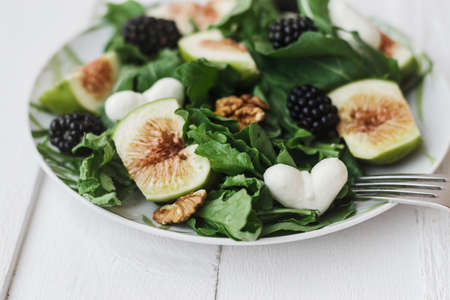 Mozzarella in the shape of heart in Salad with arugula figs blackberry and walnut on white tableの写真素材