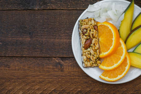 Healthy breakfast: mango, orange and muesli bar on wooden table. Copy space