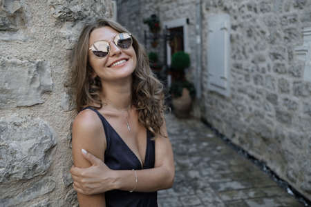 Portrait of Young curly blonde woman in long dress and sunglasses walks around the old town in Budva, Montenegro. Slow motionの写真素材