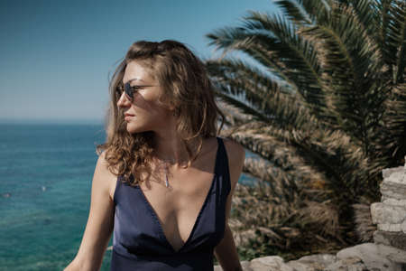 Young stylish curly blonde woman in long dress and sunglasses in long dress against the sea .の写真素材