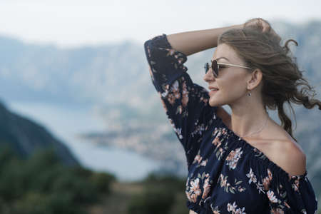 Portrait of Young stylish curly blonde woman in shorts and crochet tops and sunglasses against the backdrop of mountains and sea in Montenegro.の写真素材