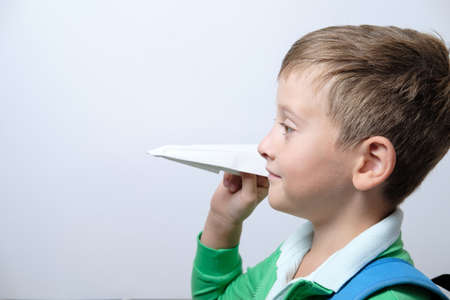 Portrait of a cute schoolboy with blue backpack and paper airplane
 on a white background. Copy spaceの写真素材