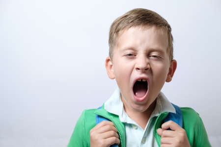 Sleepy and yawning schoolboy with blue backpack on a white backgroundの写真素材