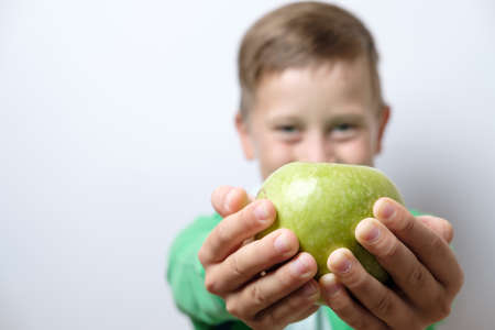 Portrait of a cute schoolboy with blue backpack and green apple on a white backgroundの写真素材