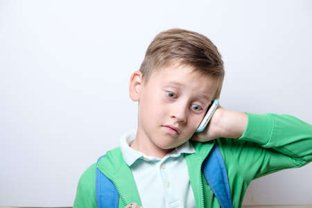 Portrait of a cute schoolboy with blue backpack and smart phone on a white backgroundの写真素材