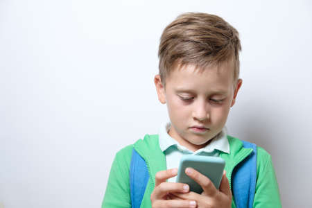 Portrait of a cute schoolboy with blue backpack and smart phone on a white background