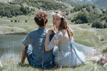Back view of Stylish Romantic couple sit by the lake against the background of the mountains.の写真素材