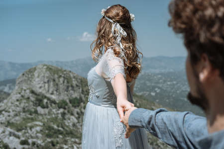 Stylish Romantic  couple against the background of the mountains. Follow me. Bride holds the bridegroom's handの写真素材