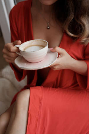 Close-up of female hands  in a red robe with cup of coffee and having lazy morningの写真素材