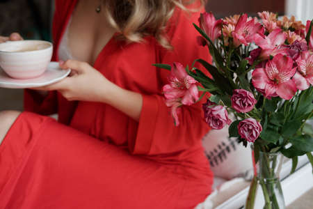Close-up of female hands  in a red robe with cup of coffee and having lazy morningの写真素材