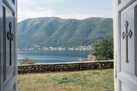 Open wooden doors with crosses of an Orthodox church overlooking the sea and mountains in Montenegroの写真素材