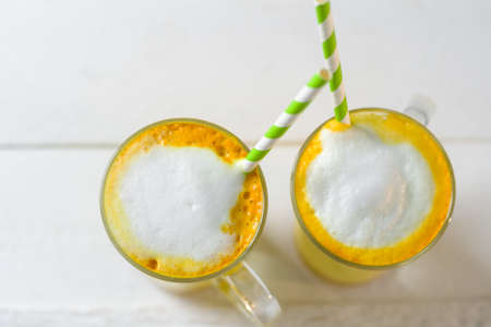 Turmeric latte or golden milk in glasses with green straw on a white table
の写真素材