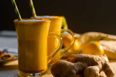 Turmeric latte or golden milk in glasses with ginger and lemons on a white tableの写真素材