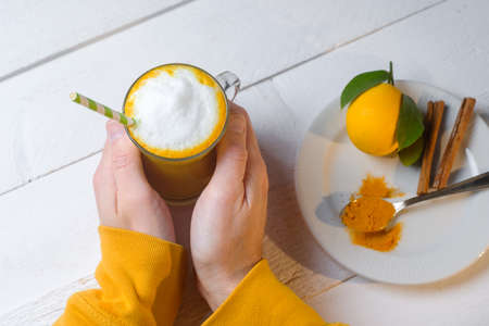Man hands with Turmeric latte or golden milk in glasses with ginger and lemons on a white table