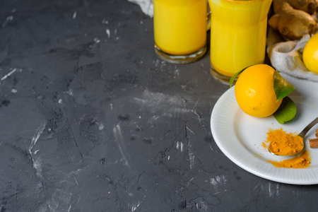 Turmeric latte or golden milk in glasses with ginger and lemons on a black  table. Copy spaceの写真素材