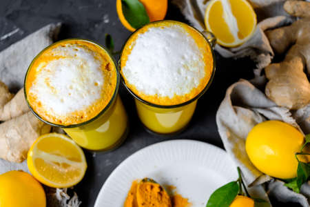 Turmeric latte or golden milk in glasses with ginger and lemons on a black  tableの写真素材