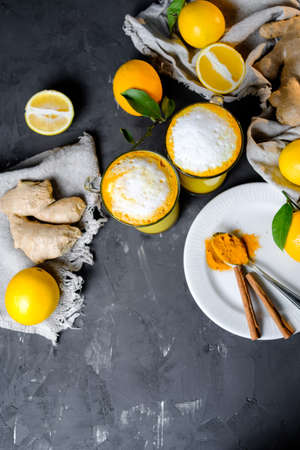 Turmeric latte or golden milk in glasses with ginger and lemons on a black  table. Copy spaceの写真素材