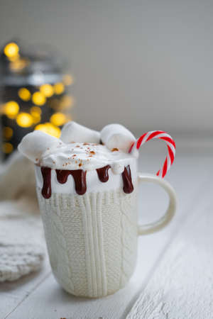 White mug with Cocoa with marshmallows and chocolate on a background of Christmas lightsの写真素材