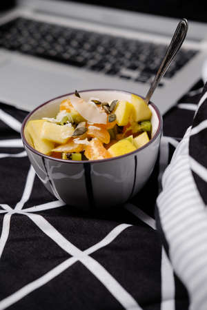 Morning in pastels: fruit breakfast and laptop on a black bedの写真素材