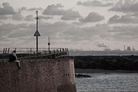 Depressed person sitting on pier  Watching industry  Cloudy atmosphere  の写真素材