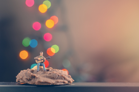 miniature man playing guitar on cookie with background of colourful bokeh lightの写真素材