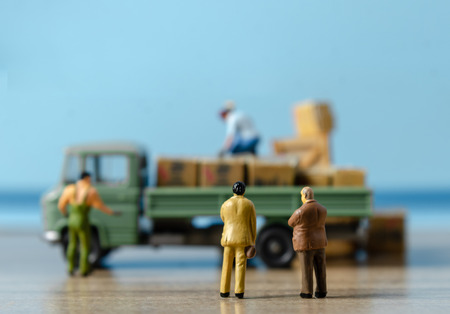 Miniature business man looking at workers carrying products goods box to container truck in distribution warehouse factory. Logistics warehouse freight transportation conceptの写真素材