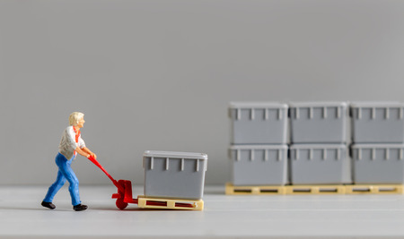 miniature warehouse man worker figure using a trolley towing hand to moving boxes