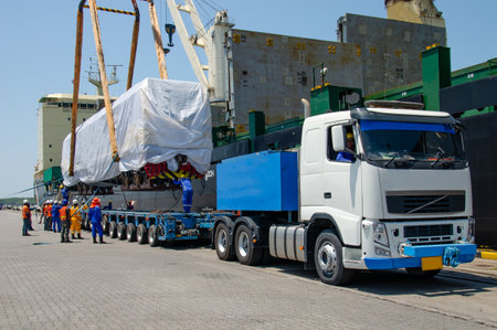 A crane on a large cargo ship docks loading a diesel-electric locomotive. Get off at Laem Chabang...