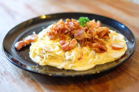The spaghetti carbonara with bacon and mushroom cream sauce on black dish set on brown wooden table for food background or texture - homemade food concept.の写真素材